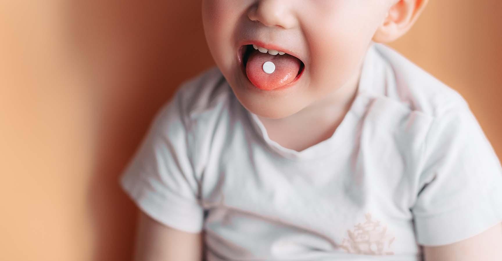 Selective focus at a white pill on a tongue of small toddler baby boy.