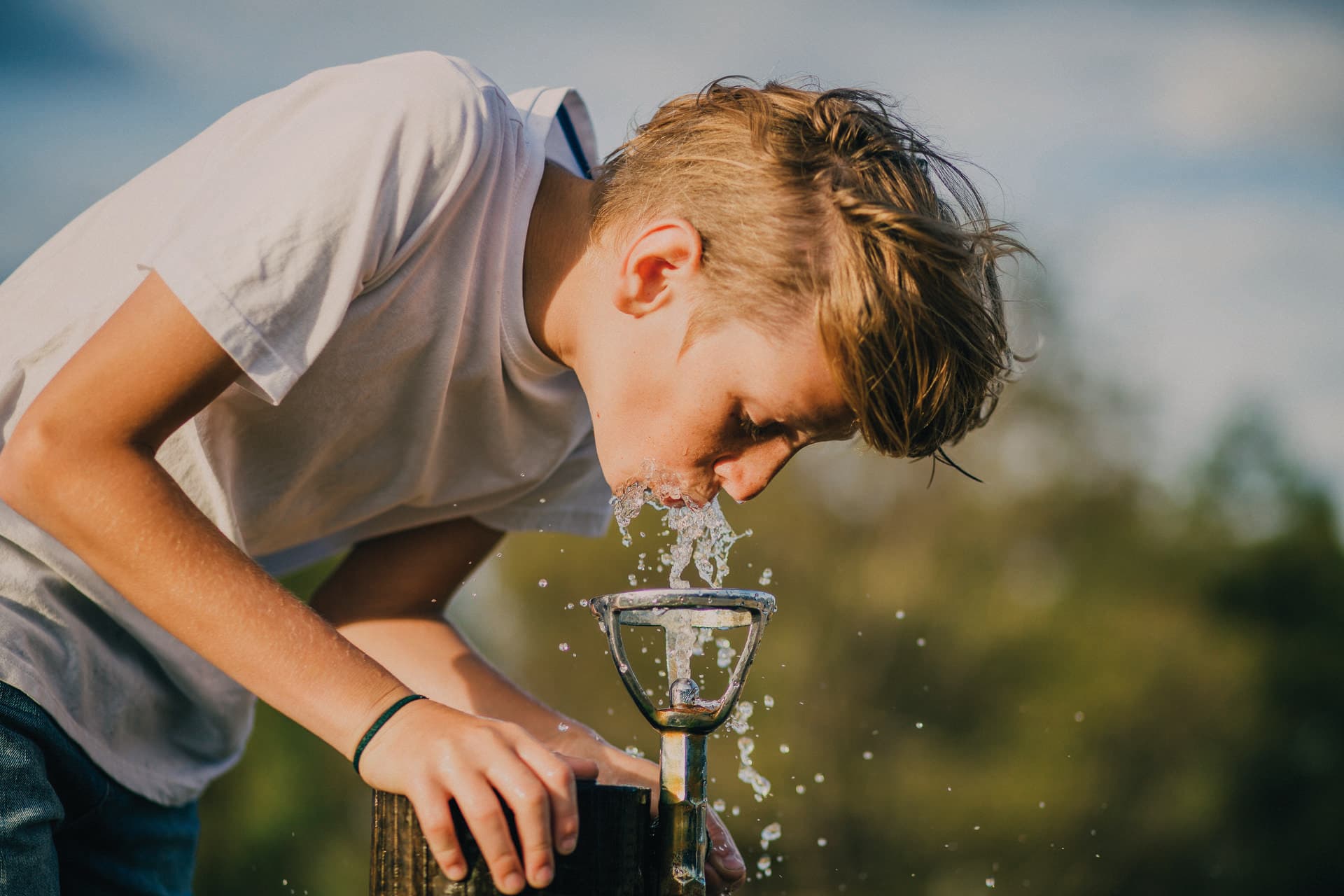 Kleiner Junge trinkt aus einem Brunnen in einem Park in Melbourne, Australien.