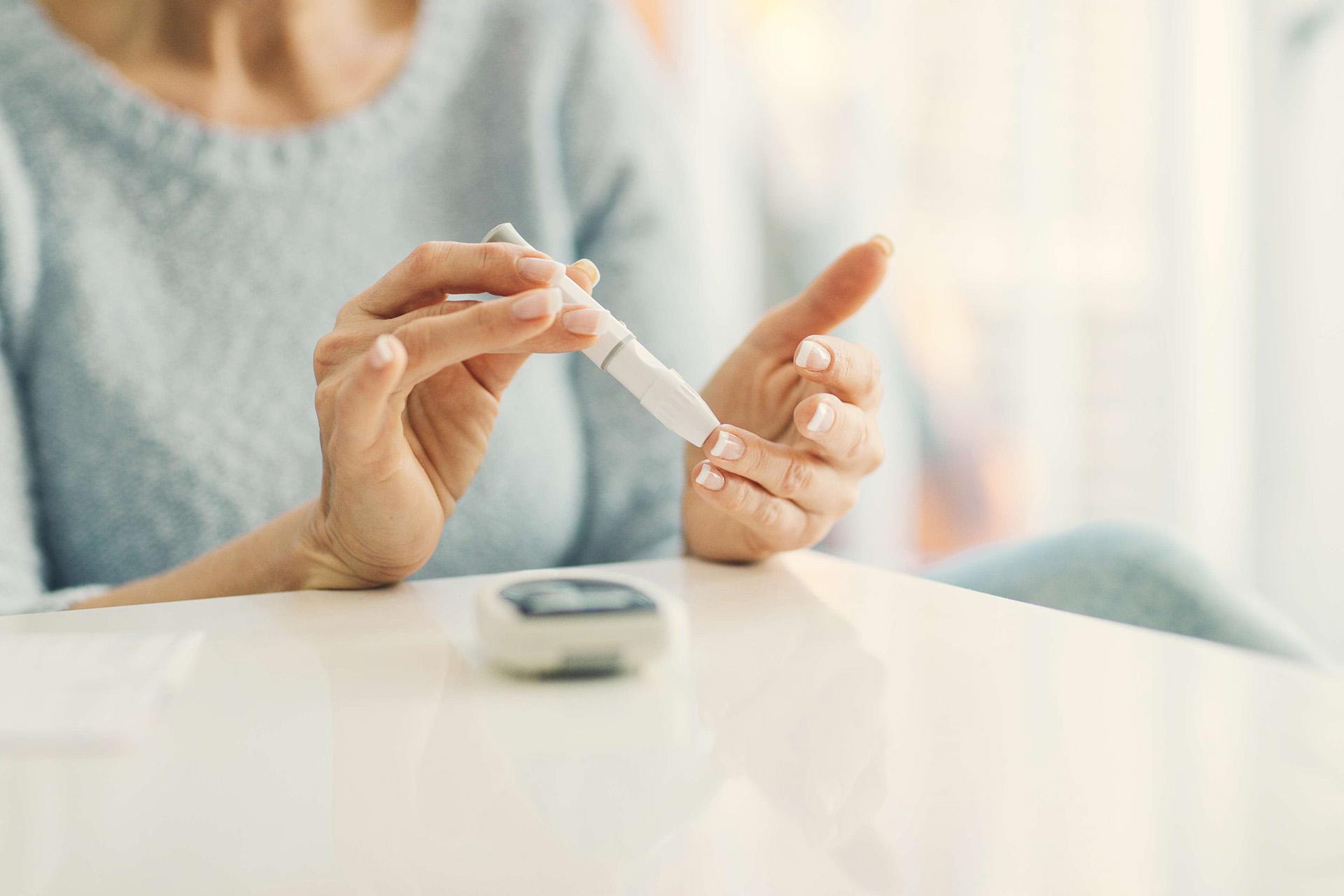 Reife Frau, die zu Hause in einem Wohnzimmer Blutzuckertest durchführt. Selektiver Fokus auf ihren Finger.