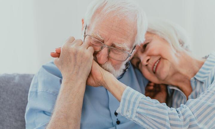 Altes verliebtes Ehepaar sitzt auf einem Sofa. Er küsst ihre Hand.