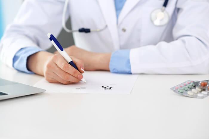 Ärztin füllt Rezeptformular aus, während sie im Krankenhaus in Nahaufnahme am Schreibtisch sitzt.