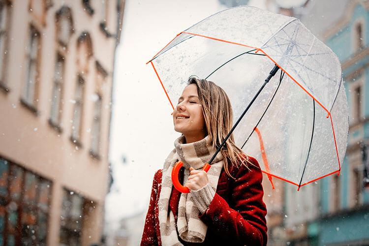 Frau mit Regenschirm steht im Regen in einer Stadt