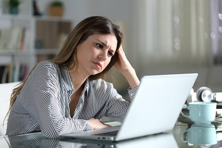 Besorgte junge Frau sitzt zuhause vor dem Laptop.
