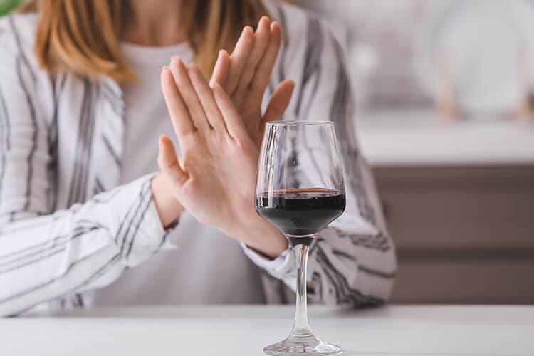 Frau verwirft die Hände vor einem Glas Wein. Alkoholverzicht.