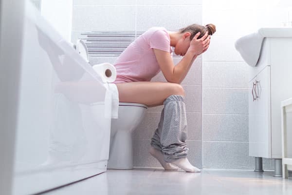 Frau mit Blasenentzündung sitzt verzweifelt auf dem Klo im Badezimmer.